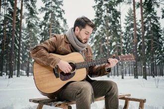 Homme jouant de la guitare acoustique sur un traîneau en bois dans une forêt enneigée nordique, évoquant l'univers musical de Kristoff dans Disney Frozen